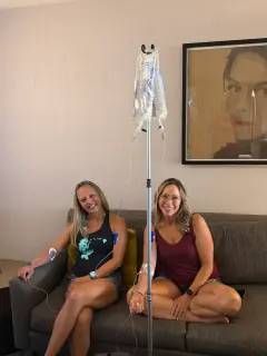 Two friends seated together on a sofa while receiving IV therapy.